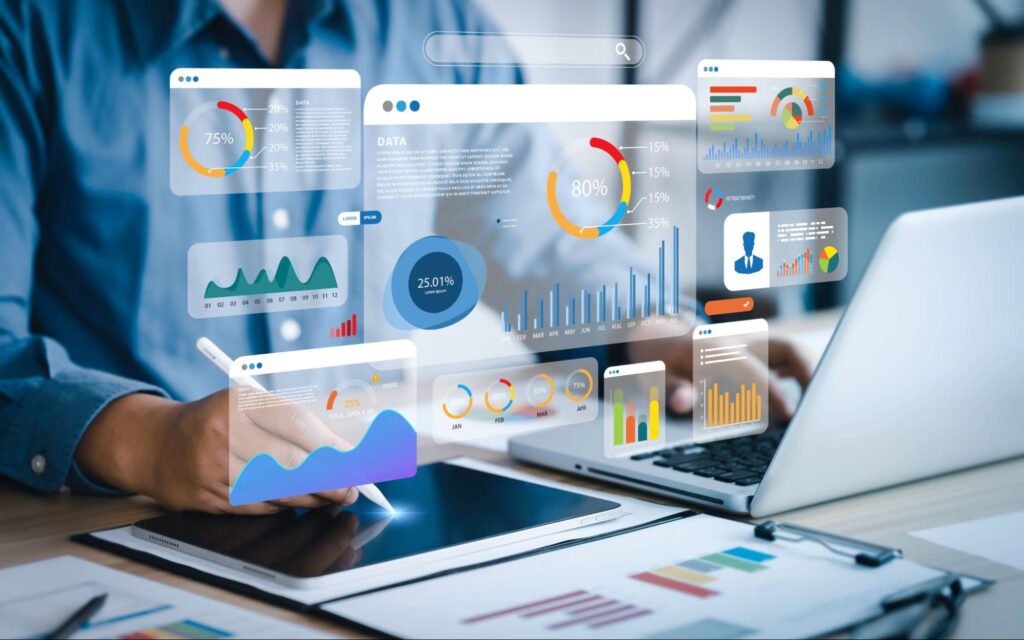 A floating digital overlay shows many colorful modules featuring graphs, data, and charts. Behind the overlay an office worker is using a stylus on their tablet while looking at their laptop.