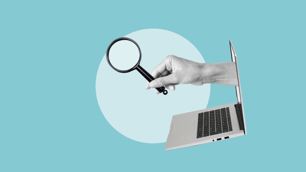 A hand holding a magnifying glass extends out of the screen of an open laptop. It looks like the hand is handing the search glass over to the invisible user.